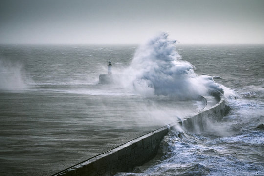 A monster wave crashes over a sea wall near a lighthouse during a storm © Matthew J. Thomas