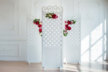 White delicate decorative wood panel in classical interior. Boudoir wedding room. Retro folding screen with flowers. Vintage ornate carved folding screen.