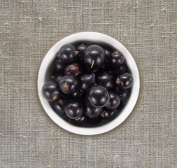 Black currants in a white ceramic bowl. Top view. Ripe and tasty currants on a linen tablecloth. 