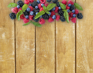 Various fresh summer berries on wooden background. Ripe blueberries, raspberries and blackberries. Berries at border of image with copy space for text.  