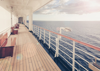Cruise ship wooden promenade deck with beautiful runrays at sunset on the open sea.