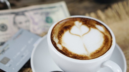 Cappuccino coffee and chocolate cookies. A cup of latte, cappuccino or espresso coffee with milk put on a wood table with dark roasting coffee beans, US bills and credit card.