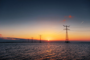 Fototapeta na wymiar electric line above water during a fantastic sunset.