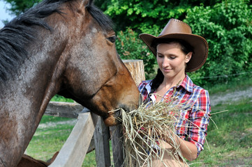 young attractive cowgirl  feeds horse in the farm