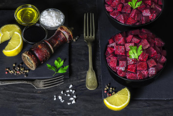 Delicious beet salad in black bowls placed with fresh lemon,olive oil, salt, balsamic vinegar,parsley and mixed pepper on dark background.Top view,copy space..