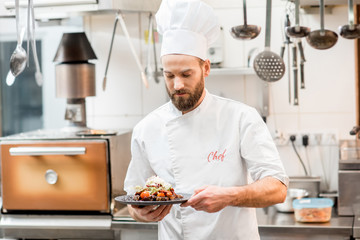 Portrait of chef cook in uniform standing with delicious dish at the kitchen