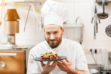 Portrait of chef cook in uniform standing with delicious dish at the kitchen