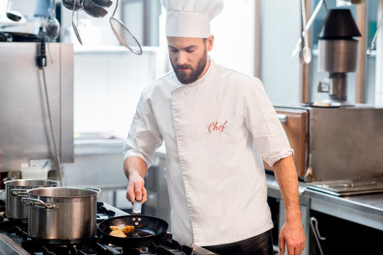 Handsome Chef Cook In Uniform Cooking Food On The Gas Stove At The Restaurant Kitchen