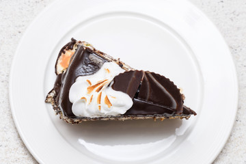 Dark chocolate cake slice with white cream, nuts and curl, close up