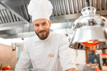 Portrait of a handsome chef cook in uniform at the restaurant kitchen - obrazy, fototapety, plakaty