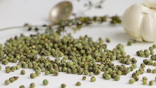 Green peppercorns - pepe verde - famous spice of italian cuisine on white table with garlic bulbs, thyme twig and spoon. Slow pan.