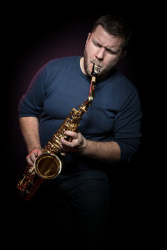 Bearded saxophonist with closed eyes hysterically plays a saxophone, isolated on a black background
