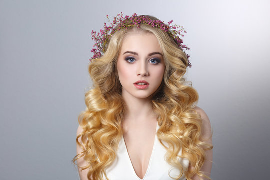 Beauty portrait of a beautiful blonde girl with chic curls and a wreath of heather isolated on a gray background.