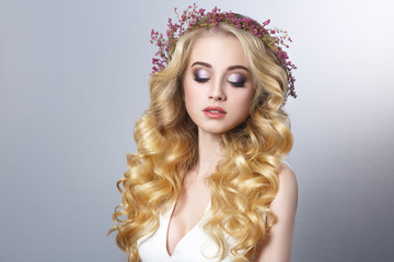 Beauty portrait of a beautiful blonde girl with chic curls and a wreath of heather isolated on a gray background.