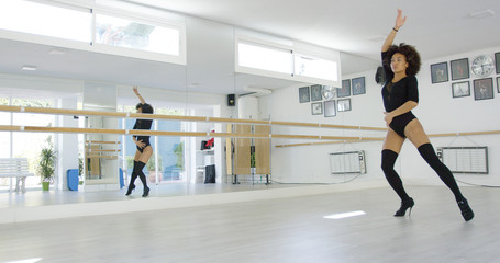 Young dancer practicing modern dancing in a bright high key dance studio striking a pose in a pair of high heeled stilettos