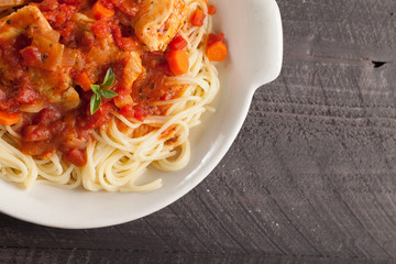 Chicken Cacciatore over pasta in white bowl on dark background top view