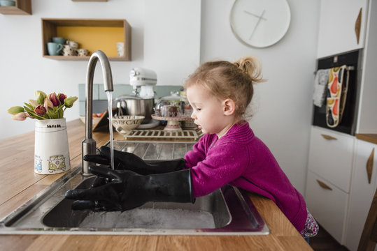 Girl wearing gloves washing hands in kitchen sink