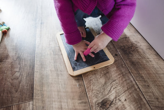 Low section of girl crouching with slate and eraser on hardwood floor