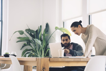 Business people using laptop while discussing at desk in office