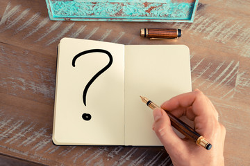 Woman hand writing a question mark on a notebook