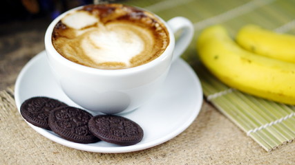 Cappuccino coffee and sweet chocolate brownies cake. A cup of latte, cappuccino or espresso coffee with milk put on a wood table with dark roasting coffee beans and bananas.