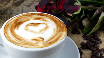 Cappuccino coffee and sweet love with hearts. A cup of latte, cappuccino or espresso coffee with milk put on a wood table with dark roasting coffee beans. Drawing the foam milk on top.