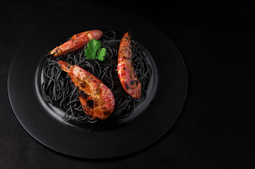 Black spaghetti with shrimps on a black background with copy space.