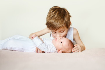 baby in white pajamas lying on his back. Older brother kisses