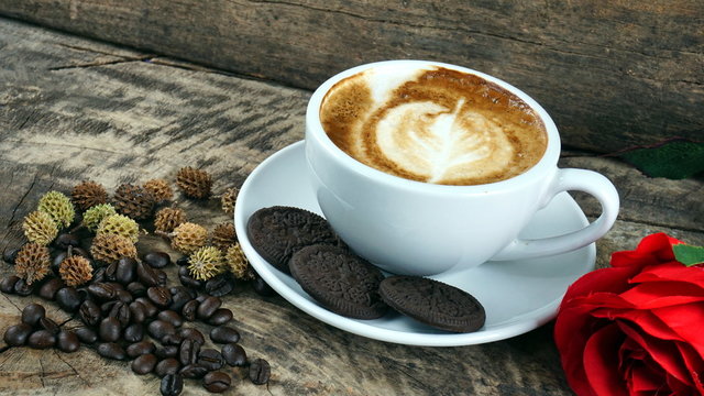 Cappuccino coffee and sweet chocolate cookies. A cup of latte, cappuccino or espresso coffee with milk put on a wood table with dark roasting coffee beans. Drawing the foam milk on top.