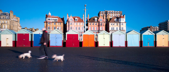 row of colourful beach huts, houses behind, man walking two with