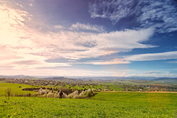 Traveler on green spring meadow. Village on sunny foothills