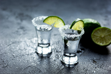 Tequila shot with lime slices and salt on dark background