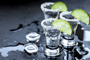 Silver tequila shots with ice and lime on black table background