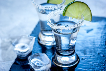 Alcohol shots with ice, lime and salt on gray stone background