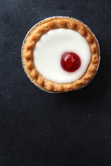 Cherry bakewell tart in foil case on dark background