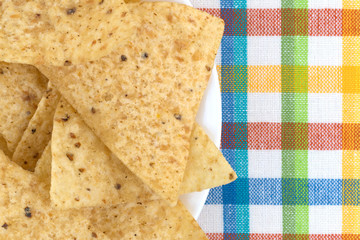 Top close view of tortilla chips on a white plate atop a colorful cloth place mat.