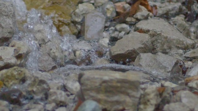 closeup slow motion clean transparent mountain river water runs over small and big grey rocks