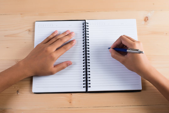 Top view of woman's hand writing on notepad.