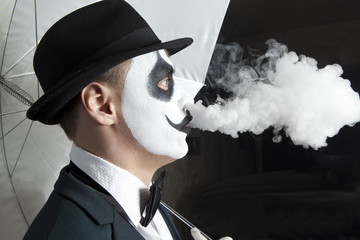 Scary evil clown wearing a bowler hat vaping