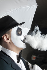 Scary evil clown wearing a bowler hat vaping
