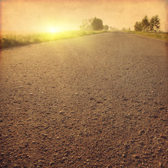 Grunge image of country asphalt road at sunset.