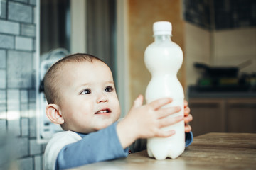 Beautiful baby reaching for milk that is on the table in the plastic bottle