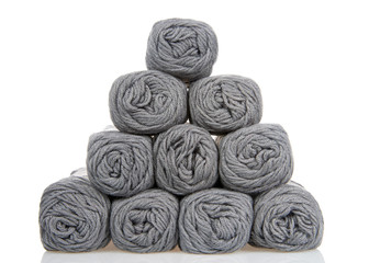 Skeins of gray colored yarn stacked into a pyramid formation on a reflective white surface, isolated on a white background.