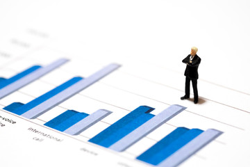 Miniature figures businessmen standing on a graph chart financial analysis review document with the team.