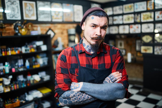 Young bearded hipster with tattooes on arms and face looking at camera