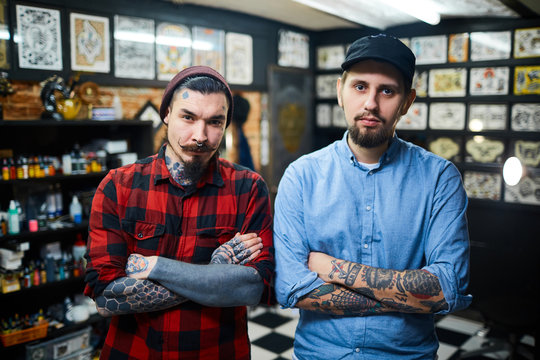 Stylish guys with crossed arms looking at camera in tattoo salon
