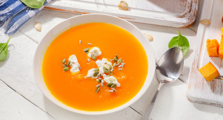 Pumpkin  soup with cream and pumpkin seeds on white wooden backg