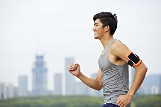 young asian man running in park against skyscrapers in the background