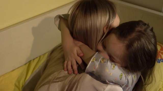 Mother hugging her daughter goodnight in bedroom.