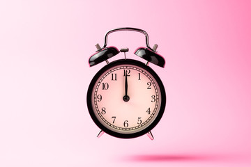 black vintage alarm clock floating on the air with pink color ba